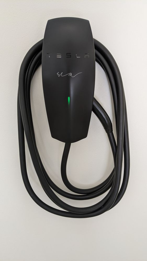 Tesla Wall Connector installed by DC Electric on a garage wall with its cable stored around the unit